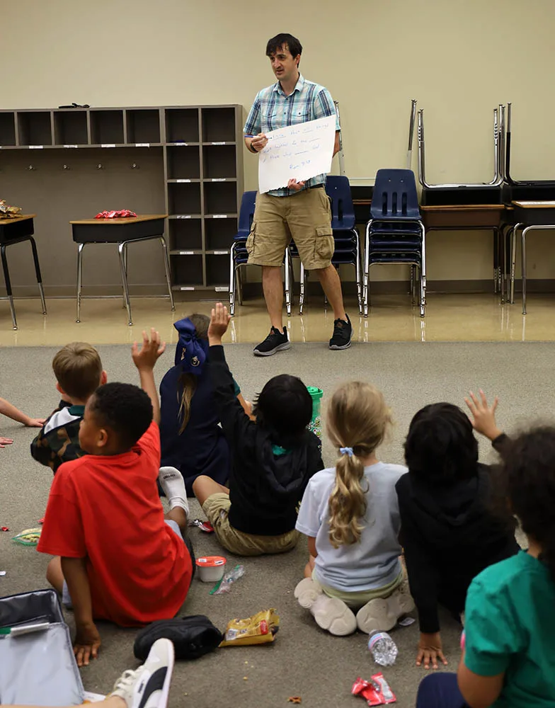 A leader teaches children seated on the floor of a classroom.
