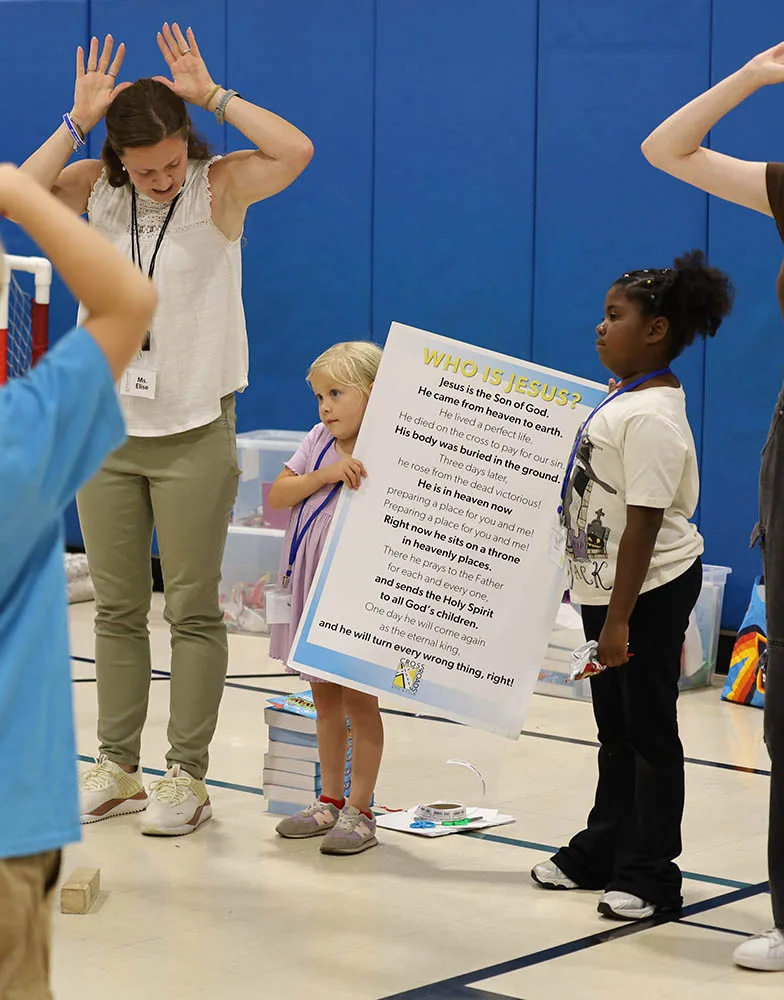 Two children hold a Who Is Jesus poster while a leader guides the activity.
