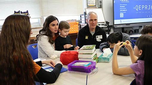 Adult mentors and children sit together around a classroom table.