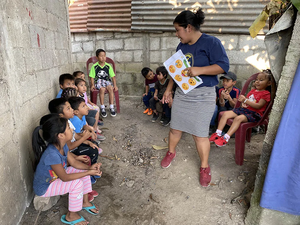 A woman teaches a small group of children outdoors.