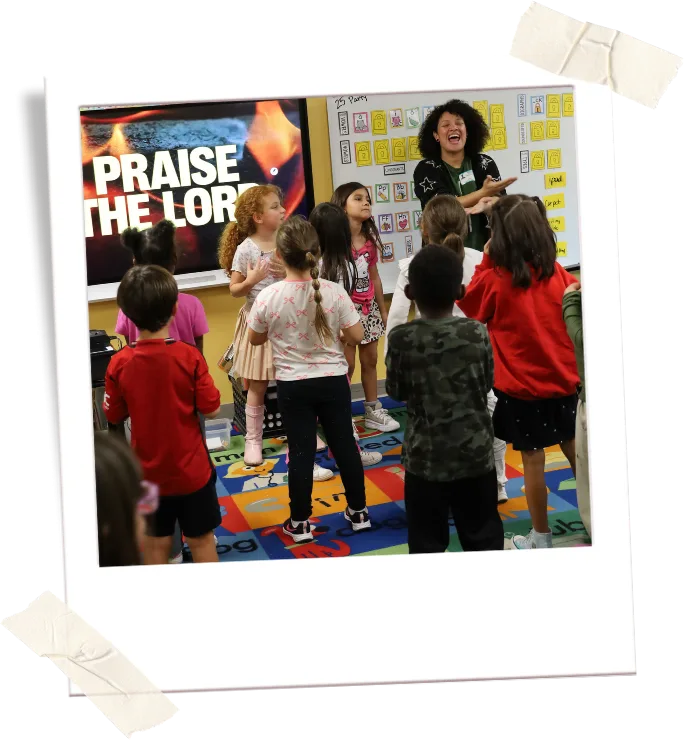 A club leader guides children through a praise activity in a classroom.