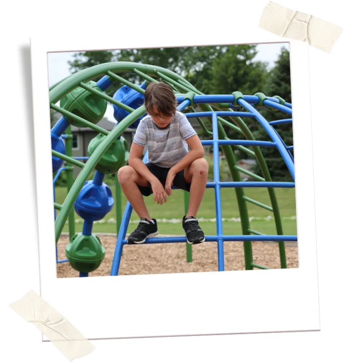 poloroid-hopeless A boy sits alone on playground climbing equipment outside a school.
