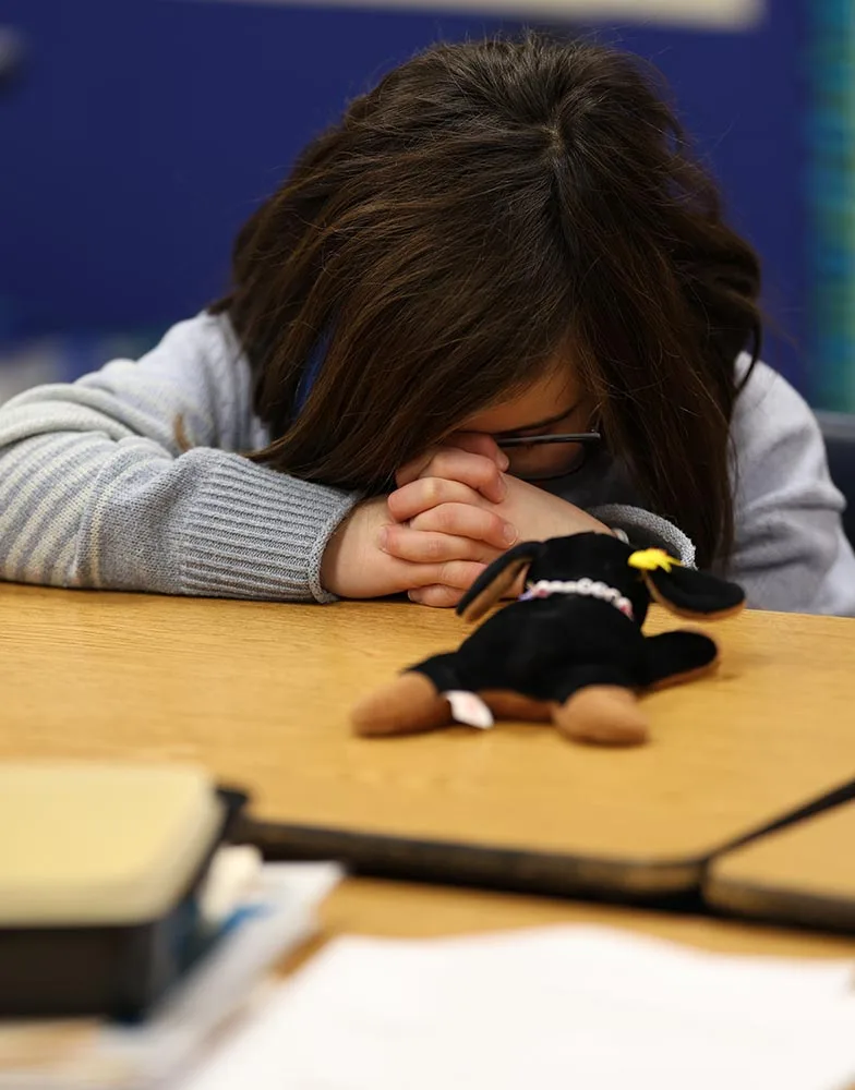 praying A girl bows her head in prayer at a classroom table during Crossroads Kids Club.