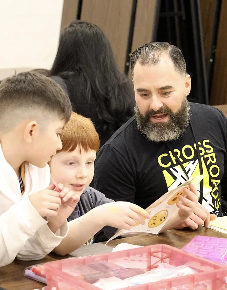 the fruit of it all Crossroads Kids Club volunteer helps two boys with an activity.